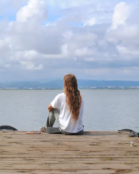 De espaldas, sentado al final de un muelle de madera, mirando el mar